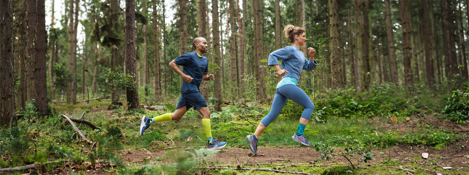 A woman and a man are running through a dense forest, wearing bandages