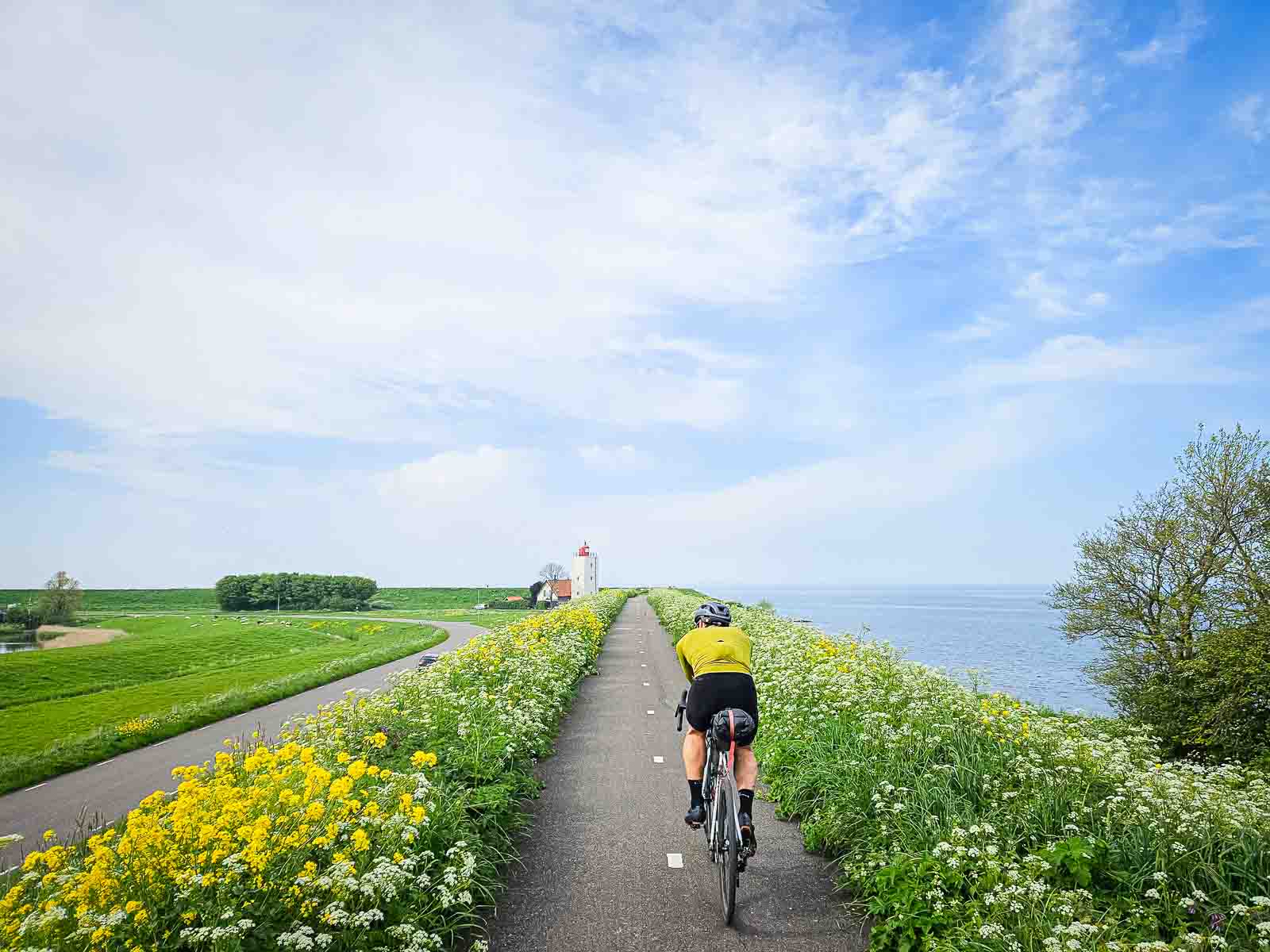A cyclist rides along a beautiful cycle path next to the sea, towards a lighthouse