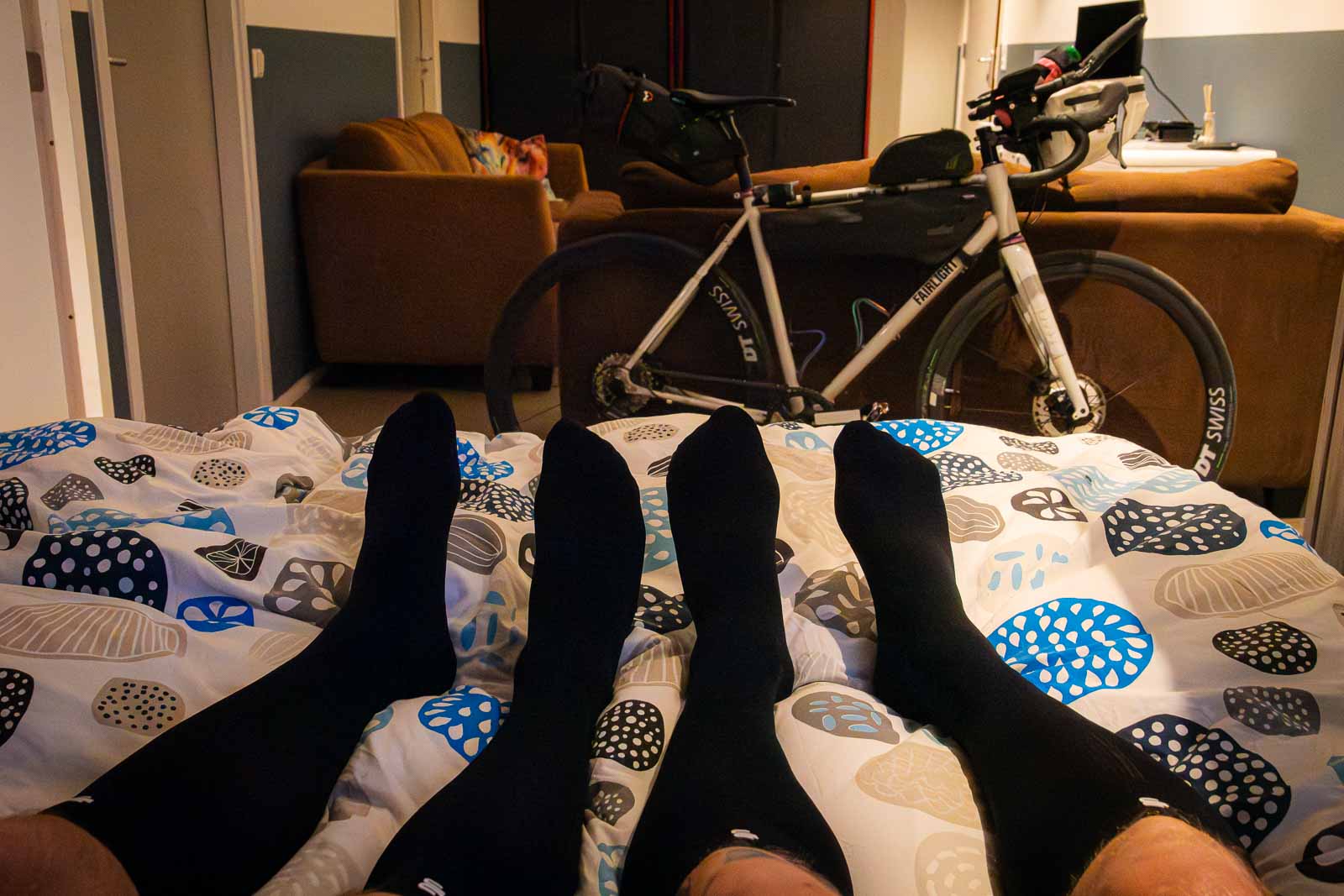 Two participants in the Race around the Netherlands lie in bed wearing recovery socks after an exhausting day.