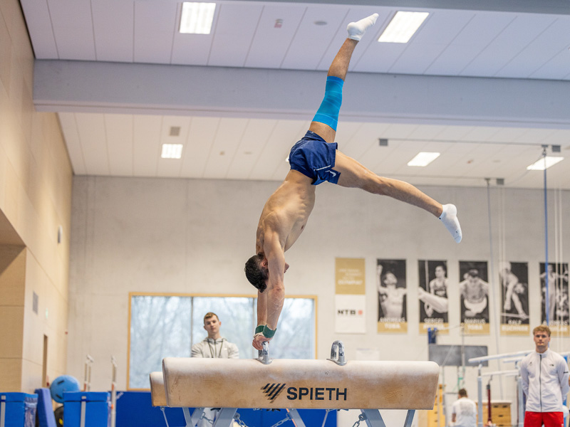 Andreas Toba in a sports hall is doing a handstand on the horse, wearing a knee brace.