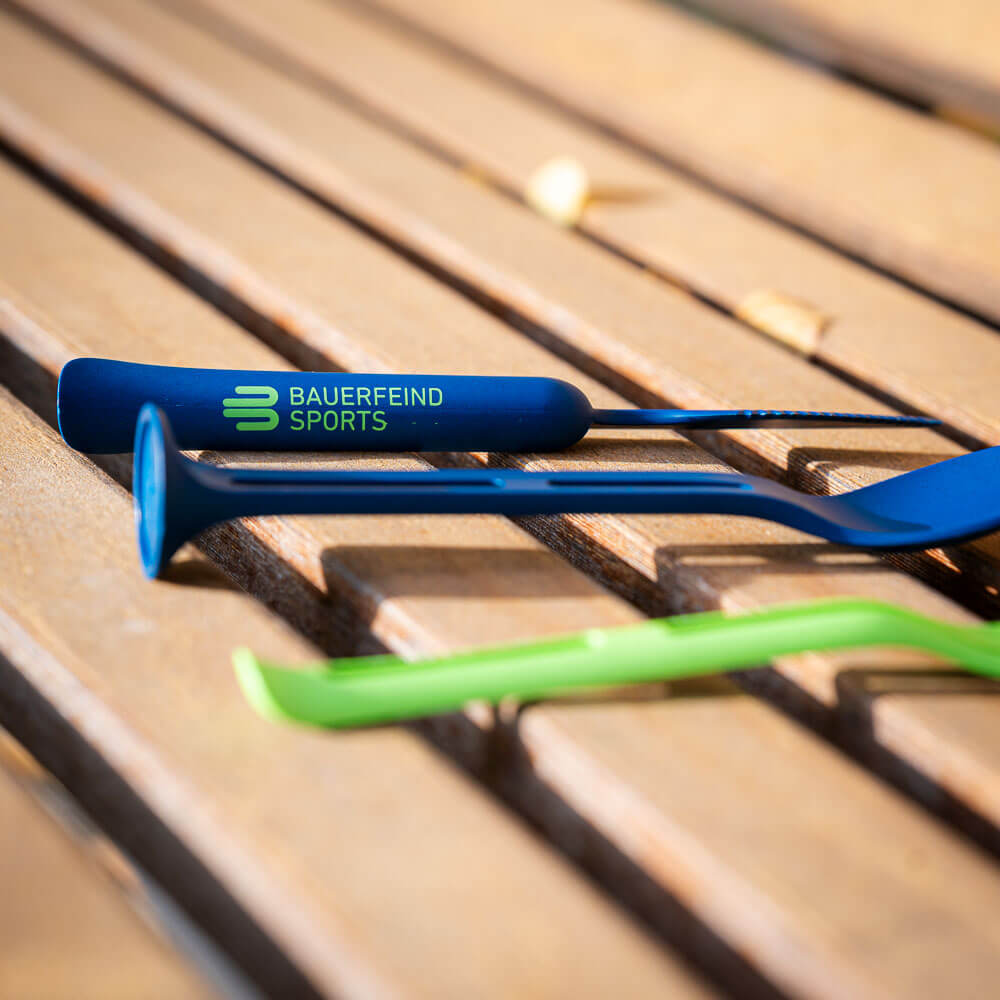 Close-up of a blue piece of cutlery on a wooden bench, with the "Bauerfeind Sports" logo visible on the handle.