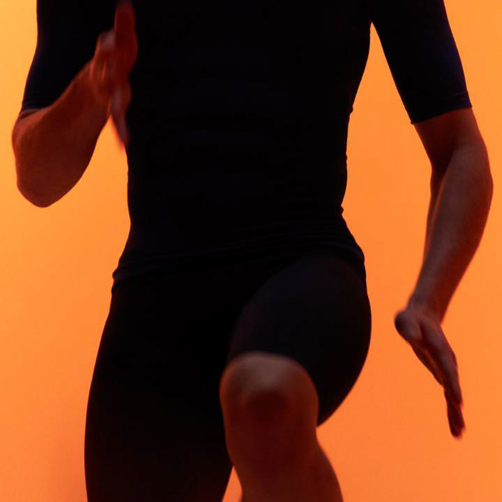 A man in sportswear does a knee lift in front of an orange background