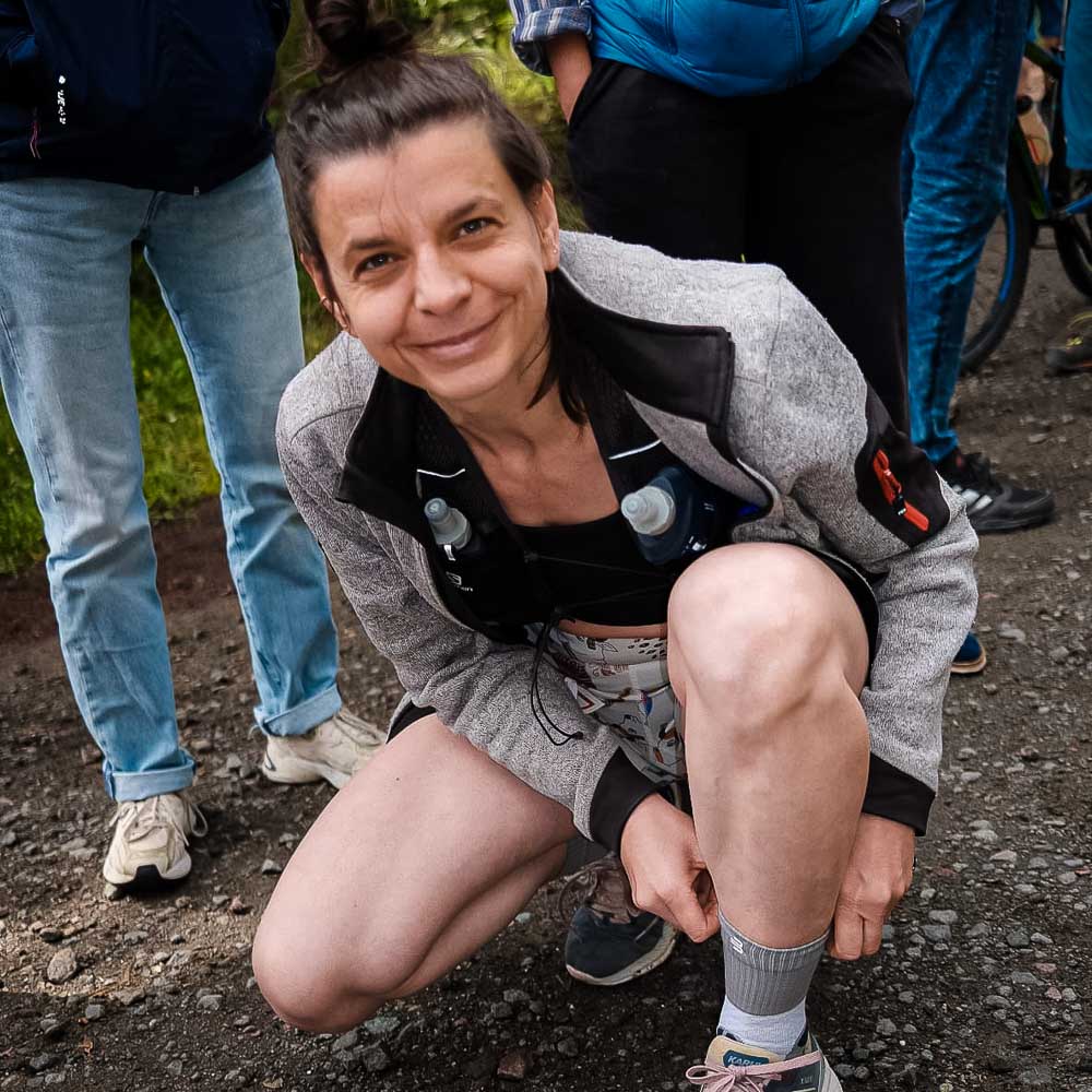 A woman smiles at the camera while adjusting her mid-length trail running socks