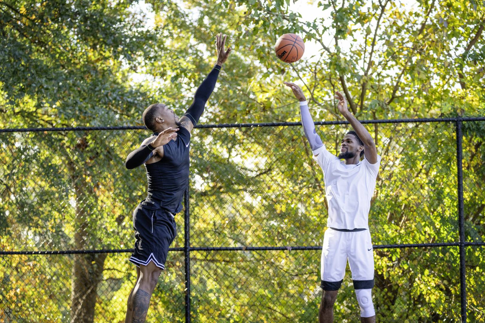 Basketball players in black game clothing tries to block his opponent in white clothes high above the ground