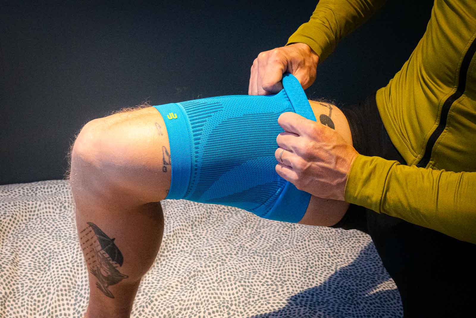 A cyclist wearing cycling clothing pulls a blue thigh compression sleeve over his thigh
