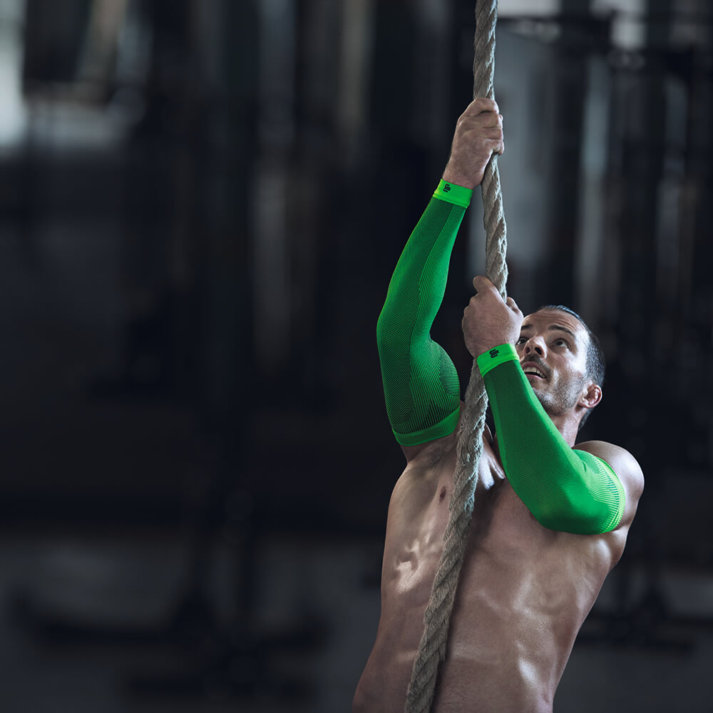 Man wearing a rope climbing is wearing green compression Sleeves for the arm