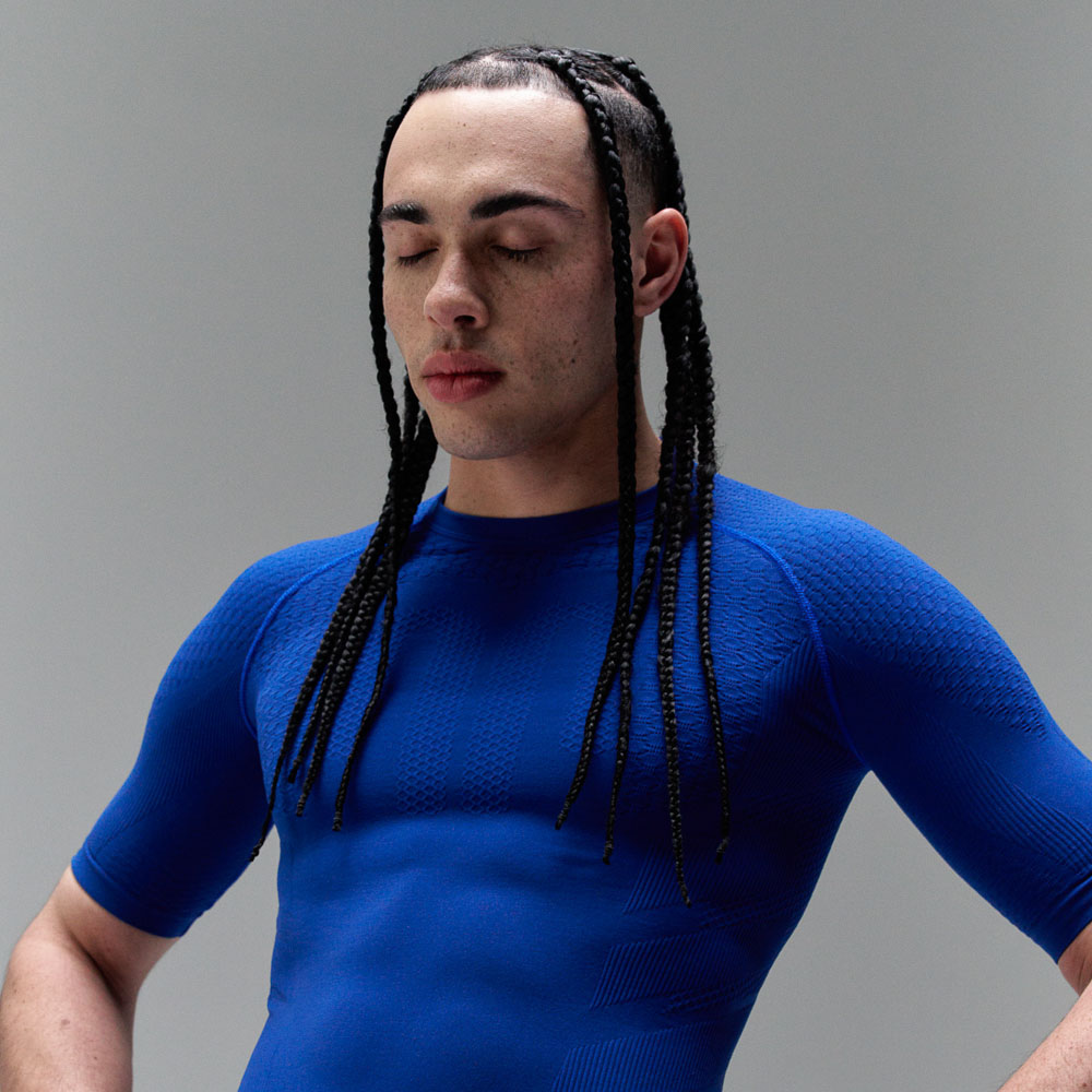 A man with braids wears a dark blue sports top, which strongly emphasises his muscles