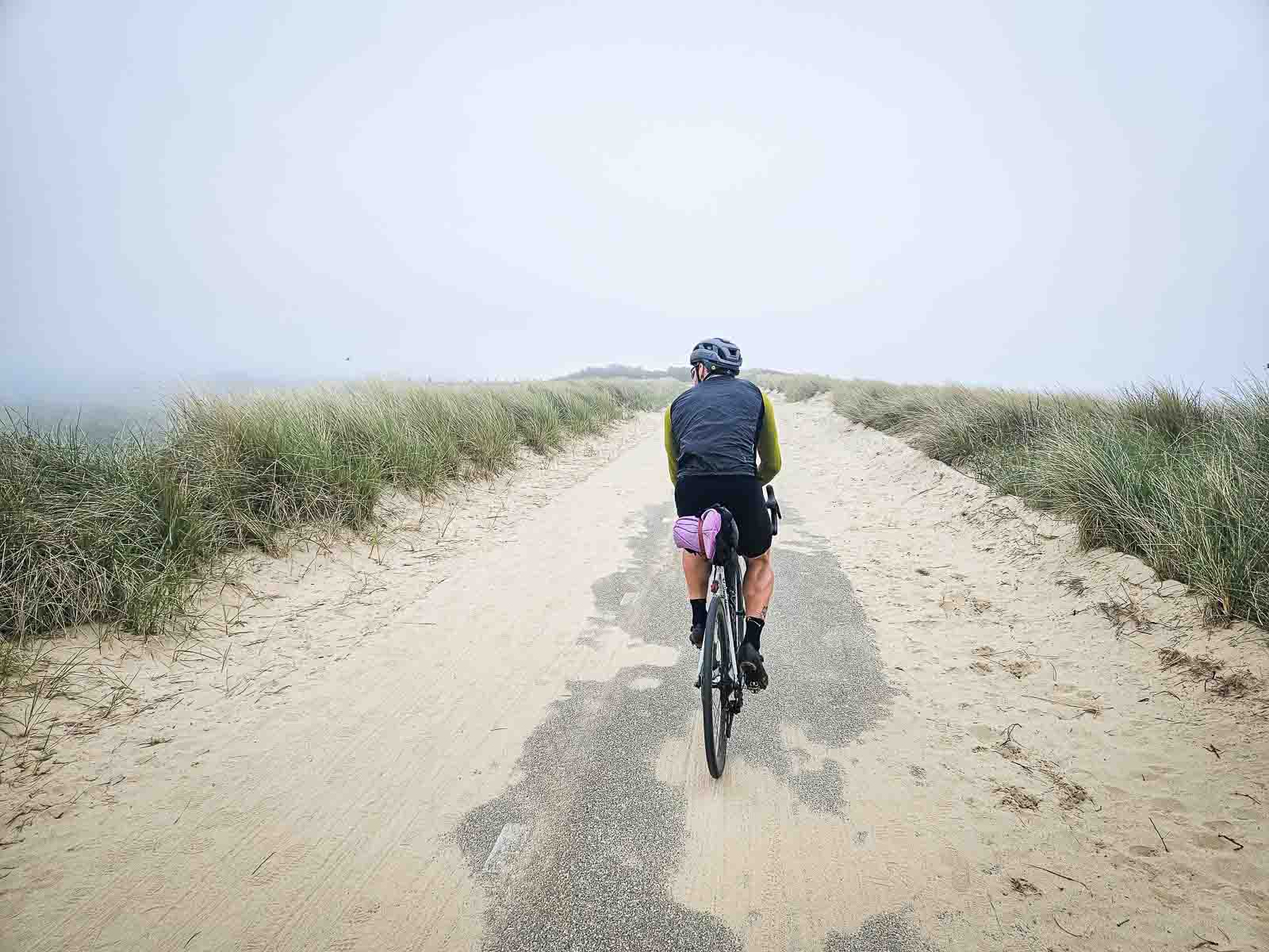 A cyclist rides over a beautiful dune road that is partially covered with sand.